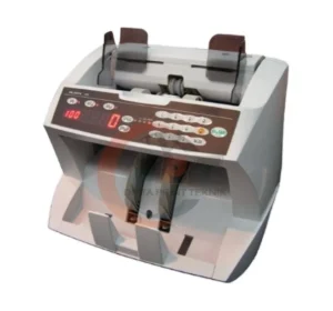 Mesin penghitung uang kertas (banknote counter) merek Glory seri GFB-800 berwarna abu-abu terang. Alat ini memiliki panel kontrol cokelat tua di bagian depan dengan tombol angka putih dan layar LED merah yang menunjukkan angka '100'. Terdapat dua slot transparan di bagian atas untuk menaruh uang.